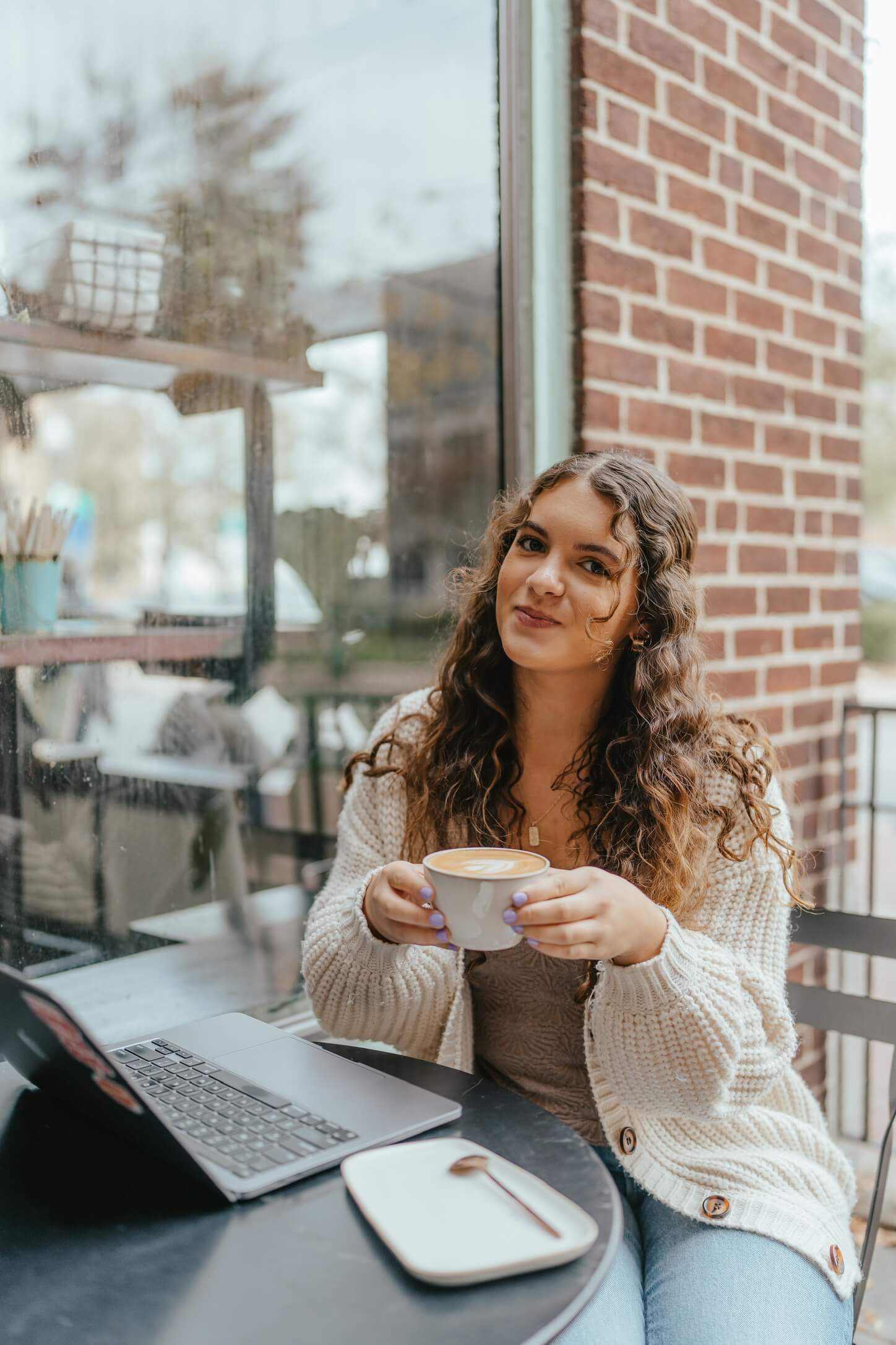 Business owner sits outside a coffee shop with a latte while she remotely works on her laptop