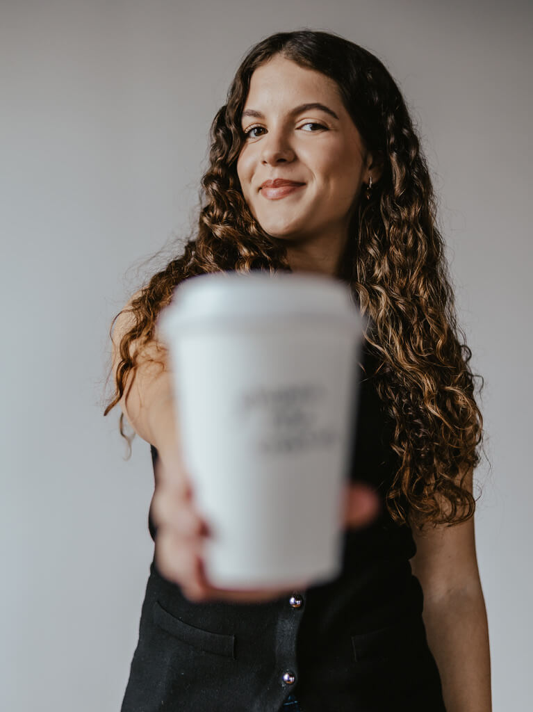 Social media manager holds up a coffee cup while smiling